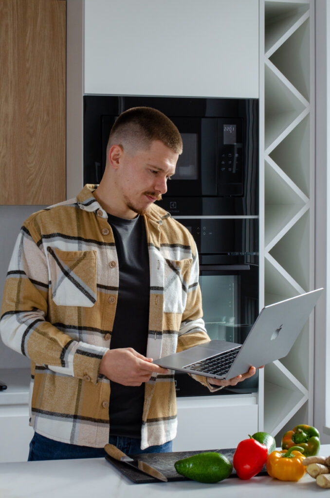 Dietetyk Oskar Radomski stoi w kuchni i trzyma w ręku laptopa.